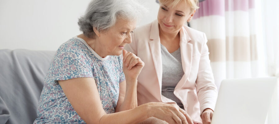 Senior woman and caregiver with laptop at home
