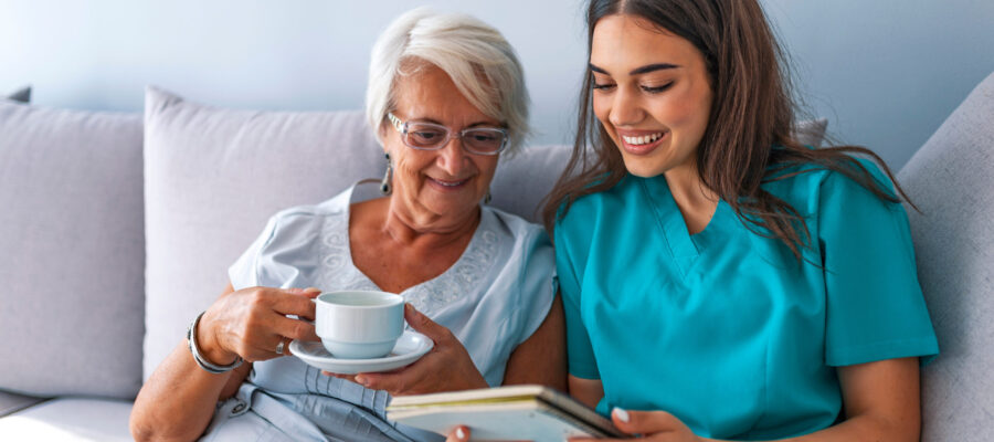 Friendly relationship between smiling caregiver in uniform and happy elderly woman. Supportive young nurse looking at elder woman. Young caring lovely caregiver and happy ward