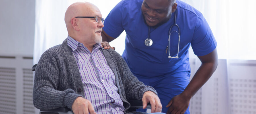 Caregiver and old man in a wheelchair. Professional nurse and patient in a nursing home. Assistance, rehabilitation and health care concept.