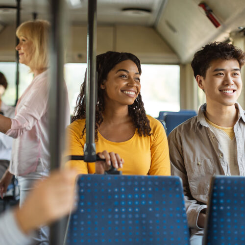 On The Road. Portrait of smiling young African American woman and Asian man taking public transport sitting on bus seat looking out of window, multicultiral passengers enjoying journey ride travel