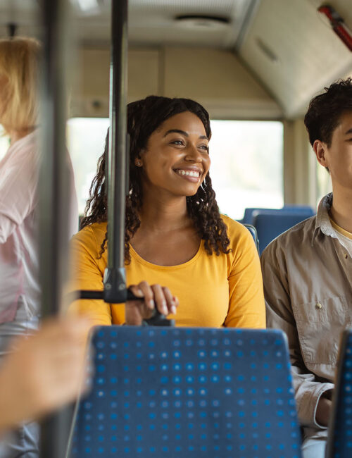 On The Road. Portrait of smiling young African American woman and Asian man taking public transport sitting on bus seat looking out of window, multicultiral passengers enjoying journey ride travel